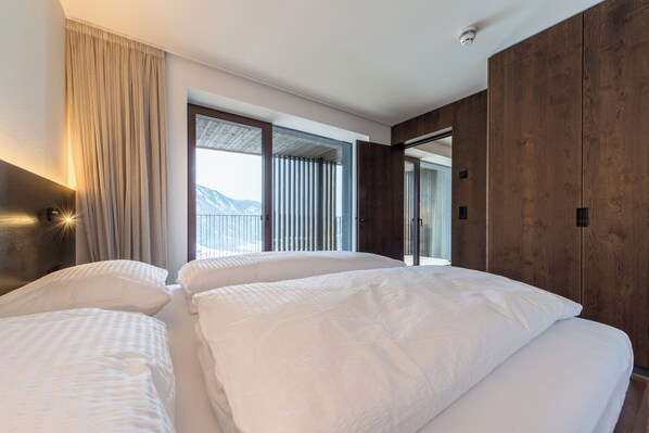 Ein Hotelzimmer mit zwei Betten, einem großen Fenster mit Vorhängen, Holzwandverkleidung und Blick auf Berge.