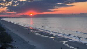 A beach with a sunset, calm sea, and a few people walking. - Pelican's Perch @ Seawatch (Myrtle Beach)