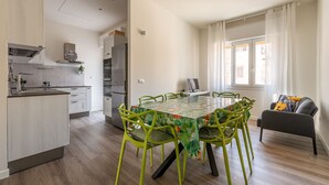 A modern kitchen with a dining area, featuring a table with chairs, a sofa, and a window with curtains.