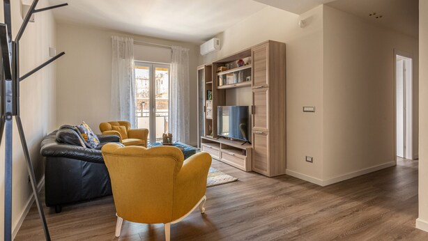 A living room with a sofa, yellow armchair, wooden cabinets, and a TV.