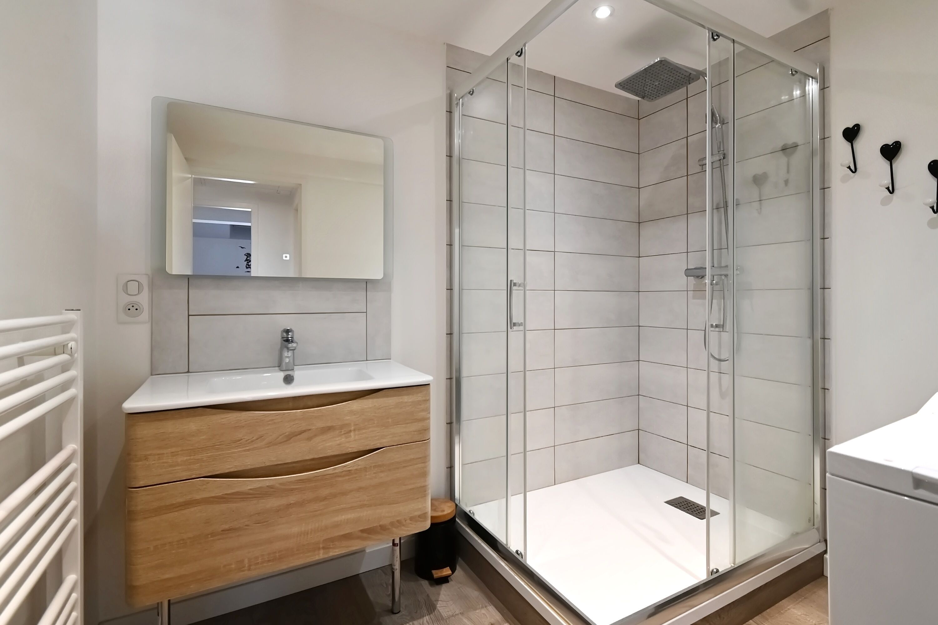 Une salle de bain moderne dotée d’une douche à parois de verre, d’un meuble-lavabo en bois avec des tiroirs, d’un lavabo blanc et d’un miroir au-dessus du meuble-lavabo.