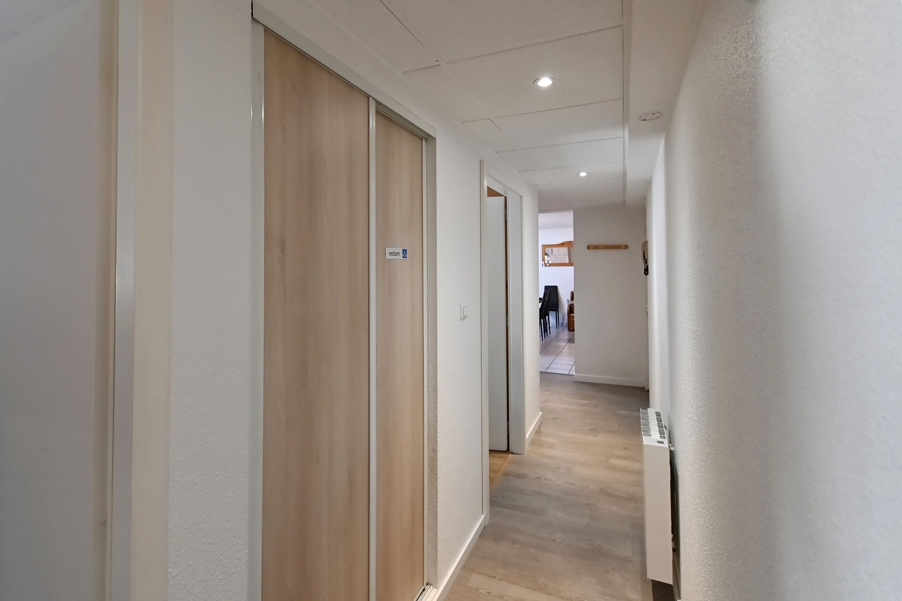 En gang med trædøre, hvide vægge og et flisegulv.