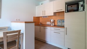 A compact kitchen with white cabinets, a microwave, a coffee maker, and a small dining area with a wooden table and chairs. - Le Nid de Ker an Aod - Appt à 100m de la plage (Benodet)