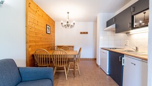 Een kleine keuken met houten lambrisering, een eettafel met stoelen, een blauwe bank en een moderne kookplaat.