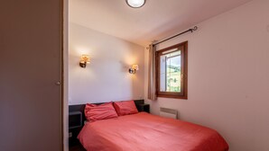 Een slaapkamer met een groot bed, twee wandlampen, een raam met uitzicht op groen en een houten vloer.