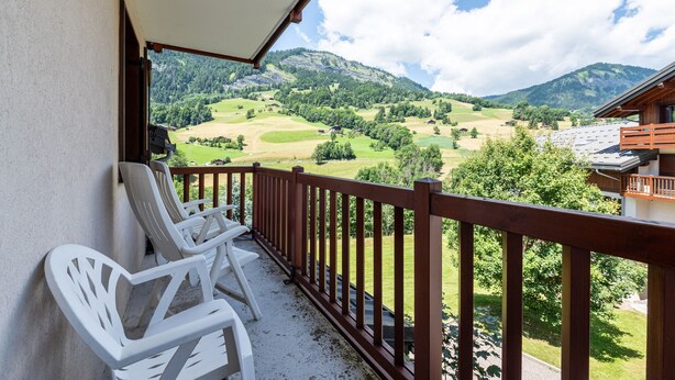 Een balkon met witte plastic stoelen en een houten hekwerk met uitzicht op een bergachtig landschap.