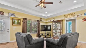 A living room with two grey sofas, a flat-screen TV, a ceiling fan, and a window with curtains. - Tremendous Family Home on the Curve! 3-bedrooms close to the lake and amenities (Brookeland)