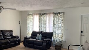 A living room with a black leather sofa, a smaller sofa, a glass vase, and patterned curtains. - Pool Heated House - Near beach in Port Charlotte (Port Charlotte)