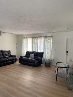 Ein Wohnzimmer mit einer schwarzen Ledersofa, einem kleineren Sofa, einer Glasvase und gemusterten Vorhängen.
