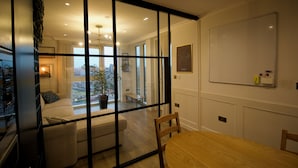 Ein modernes Wohnzimmer mit Glastrennwand, einer Couch, einem Holzesstisch und einer Tafel an der Wand.