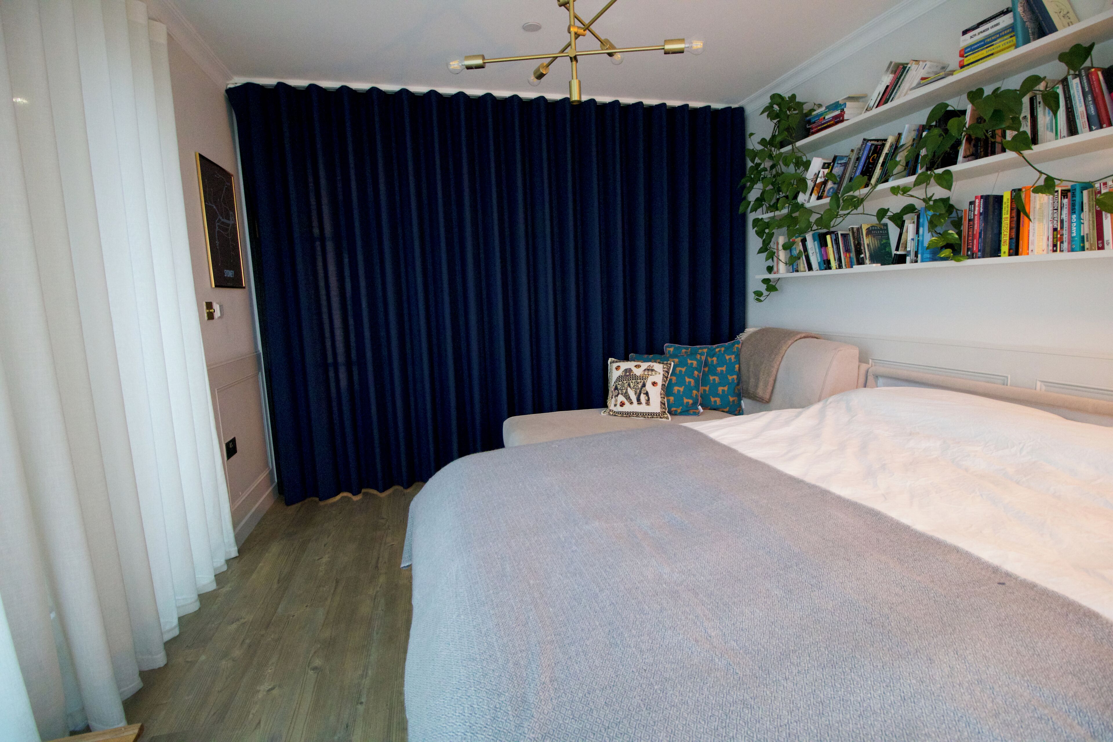 Ein Schlafzimmer mit einem Bett, einem Bücherregal und einem großen Fenster mit Vorhängen.