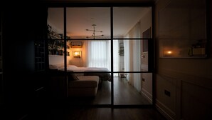 Ein schwach beleuchteter Raum mit einem Bett, einem kleinen Tisch und einem Bücherregal.