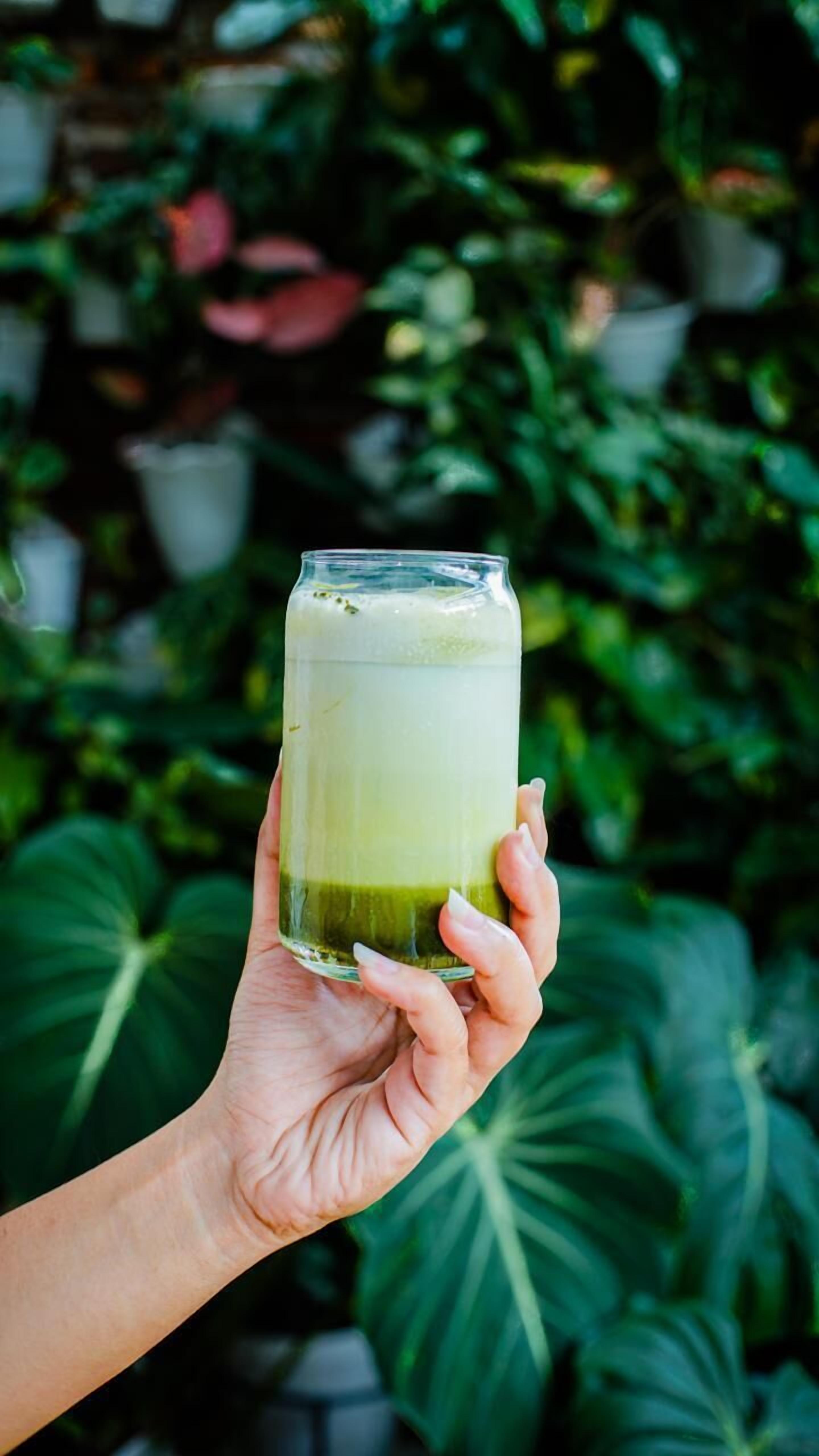 Een hand die een glas groene smoothie vasthoudt.