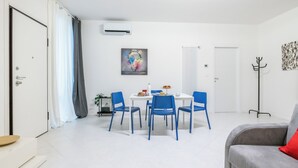 Una habitación moderna y luminosa con una mesa de comedor y sillas, un sofá gris y un equipo de aire acondicionado blanco en la pared.