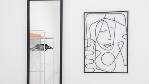 Una obra de arte abstracta enmarcada con un diseño minimalista, una pared blanca y un espejo con marco de metal que refleja una escalera.