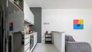 Una cocina compacta con refrigerador, estufa y pileta. Hay una cafetera y un cartel que dice 
