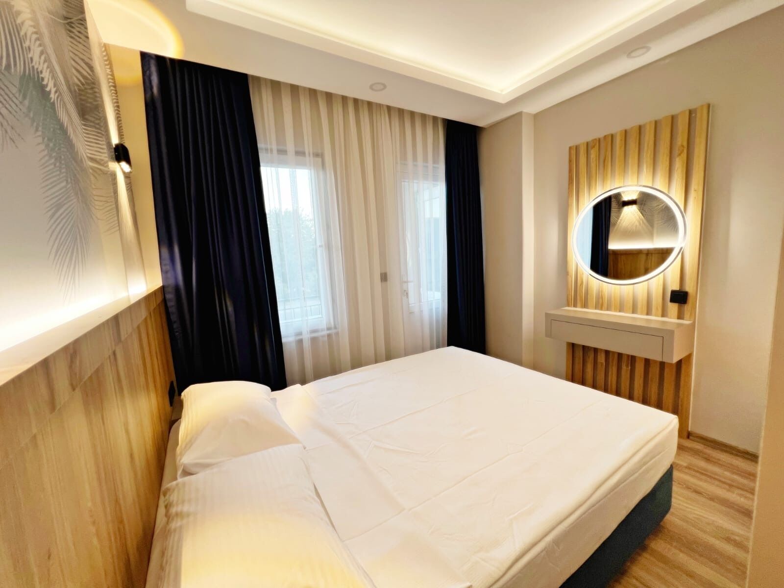 A hotel room with a bed, a mirror, and a window with curtains.