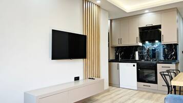 Una cocina moderna con televisor de pantalla plana montado en la pared, horno empotrado y comedor con mesa y sillas de madera.