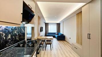 A modern kitchen with a dining area, a living space with a sofa, and a TV mounted on the wall.