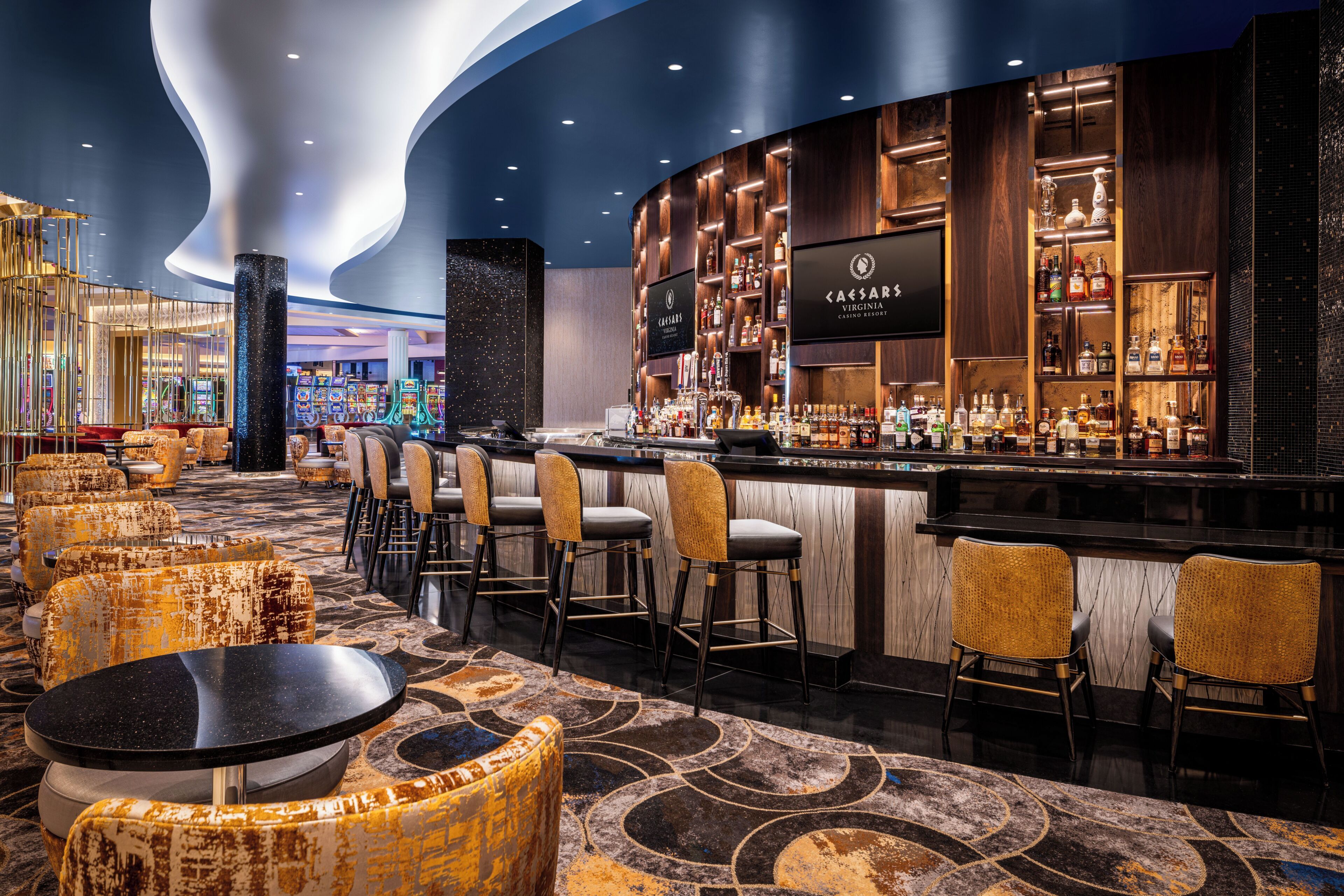 Zona de bar moderna con techo curvo, taburetes y una variedad de botellas de licor.