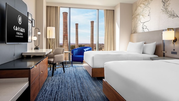 A hotel room with two beds, a desk, a chair, and a TV displaying the Caesars Virginia Casino Resort logo. - Caesars Virginia Hotel & Casino - A Caesars Rewards Destination (Danville)