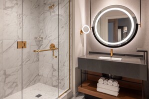 A modern bathroom with a glass-enclosed shower, a round mirror with a light, and a wooden vanity with towels. - Caesars Virginia Hotel & Casino - A Caesars Rewards Destination (Danville)