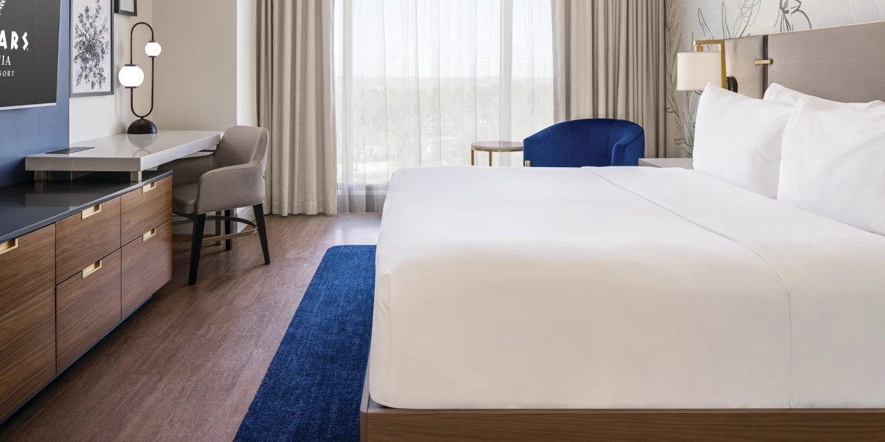 A hotel room with a large bed, a desk, a chair, and a small table.