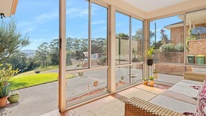 A sunlit room with large sliding glass doors, a wicker sofa, and a small table with potted plants.