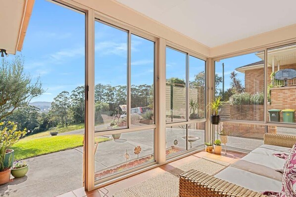 A sunlit room with large sliding glass doors, a wicker sofa, and a small table with potted plants.