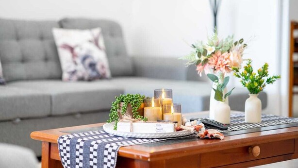 A cozy living room with a grey sofa, a wooden coffee table with candles, a remote control, and decorative vases.