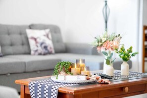 A cozy living room with a grey sofa, a wooden coffee table with candles, a remote control, and decorative vases.