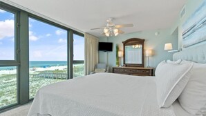 Een slaapkamer met een groot bed, een plafondventilator, een televisie, een dressoir en uitzicht op het strand.