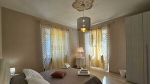 Une chambre à coucher comprenant un lit, une lampe de chevet, des rideaux, un luminaire suspendu et une armoire.