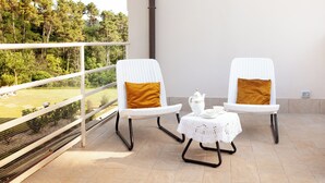 Un balcon avec deux fauteuils en osier blancs, chacun agrémenté d’un coussin de couleur moutarde, et une petite table recouverte d’une nappe blanche.