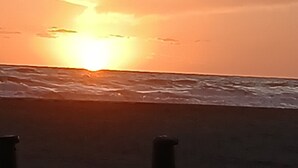 Une plage au coucher du soleil, avec du sable et deux poteaux.