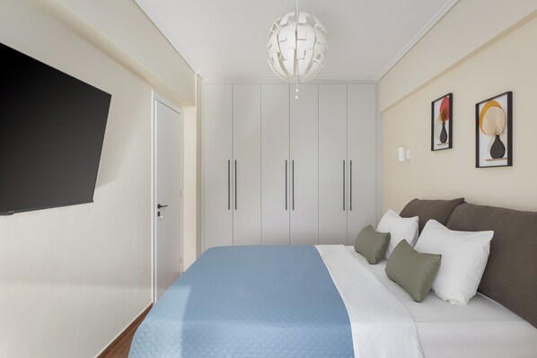 Un dormitorio con cama, televisor montado en la pared y armario.