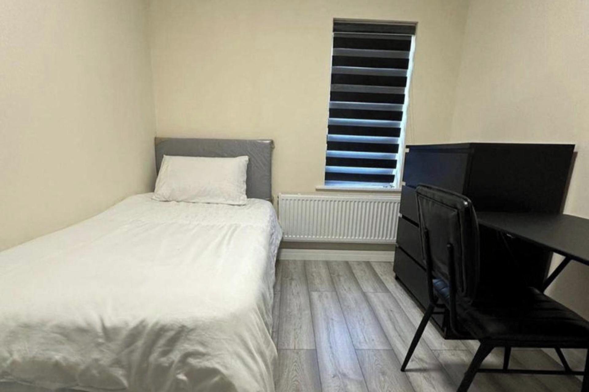 A small, sparsely furnished room with a bed, a desk, and a radiator.