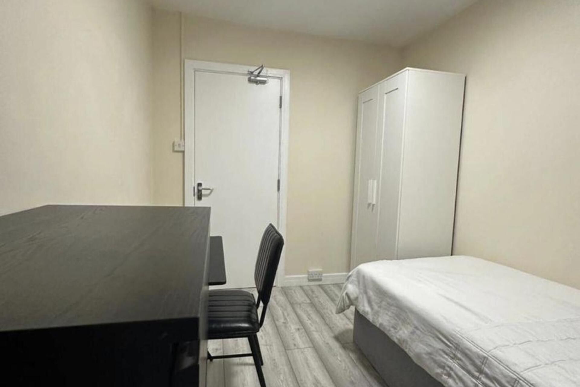 A small, simple room with a bed, a desk, and a chair.