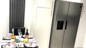 Een eethoek met een tafel gedekt voor twee personen, een koelkast en een zwarte stoel.