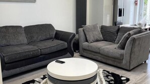 Een moderne woonkamer met twee grijze banken, een ronde salontafel en een kamerbreed tapijt met een patroon.