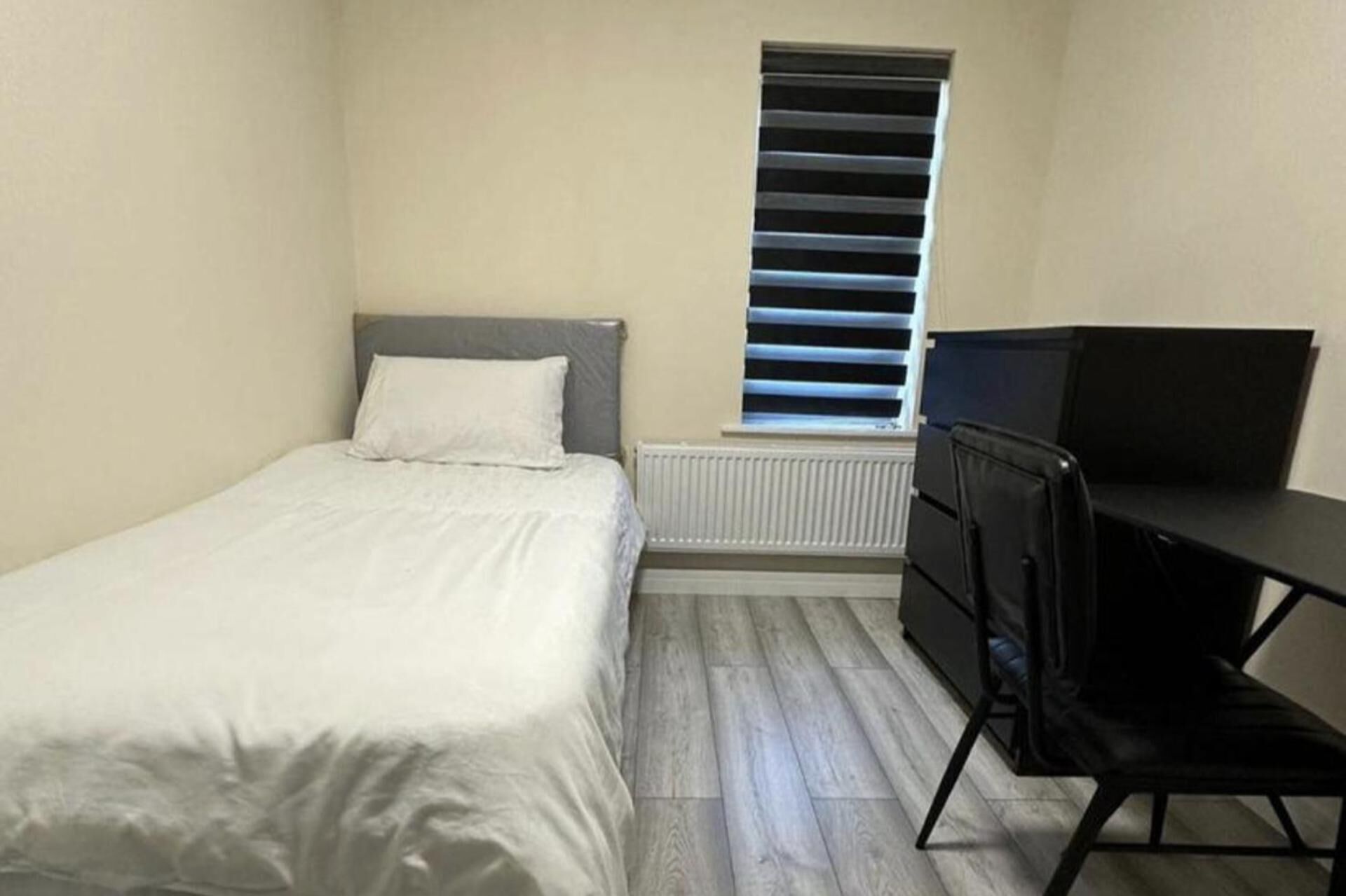 Una habitación pequeña y sencilla con cama, escritorio y radiador.