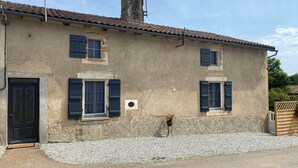 A two-story building with a tiled roof, a chimney, and a small garden area with gravel and a potted plant.
