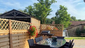 An outdoor patio with a round table and chairs, a grill, and a wooden fence.