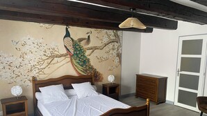 A bedroom with a wooden bed, a peacock mural, a dresser, and a door.