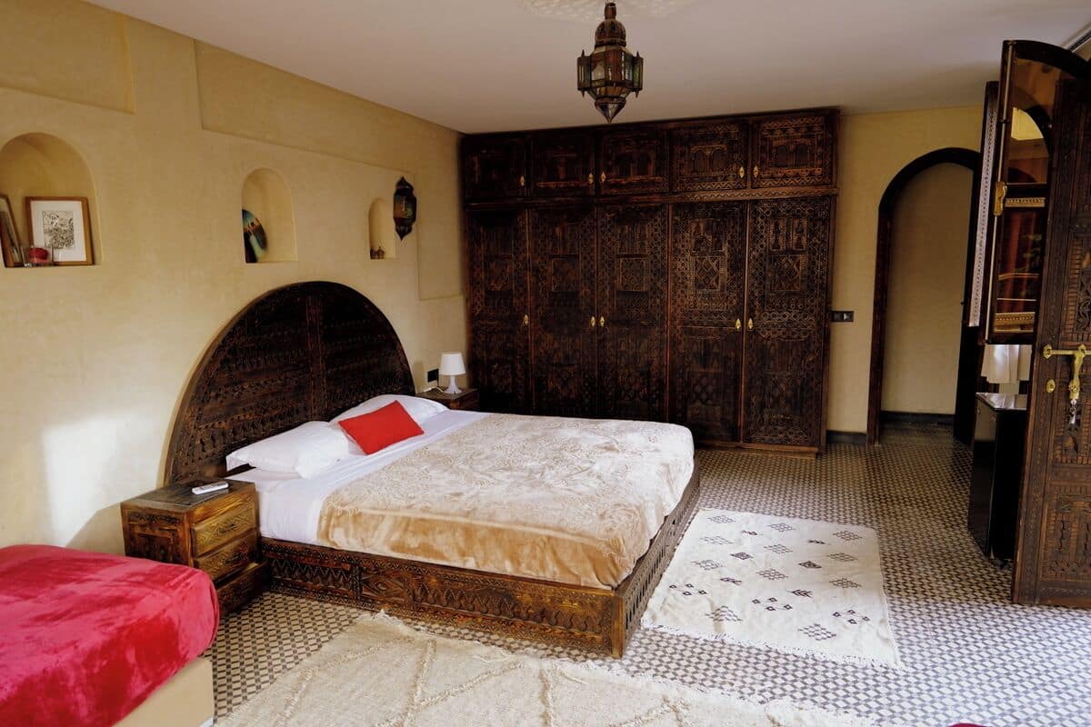 Quarto com uma cama grande, guarda-roupa de madeira e um tapete estampado.