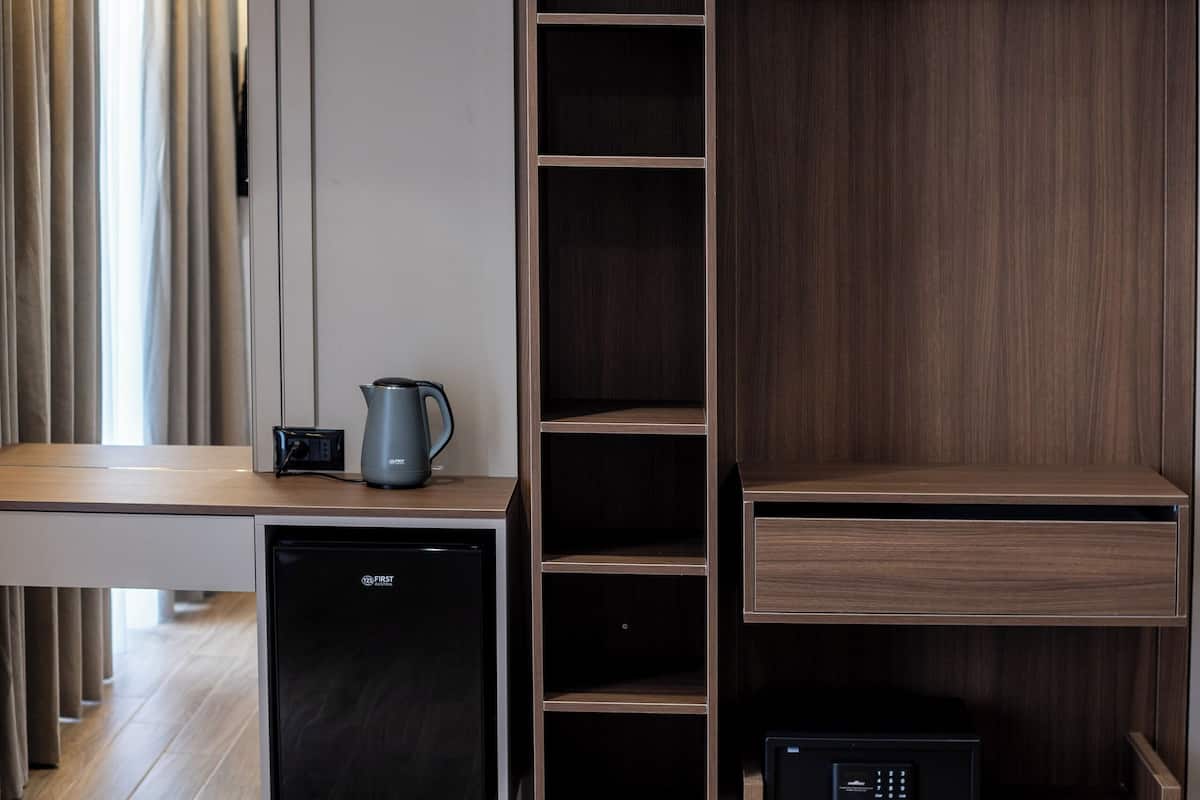 A modern hotel room with a wooden desk, a small refrigerator, a coffee maker, and a built-in wardrobe with multiple compartments.