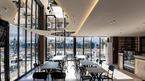 A modern restaurant with a long communal table, high ceilings, and large windows offering a view of the city. - Bolt Boutique Hotel (Shënkoll)