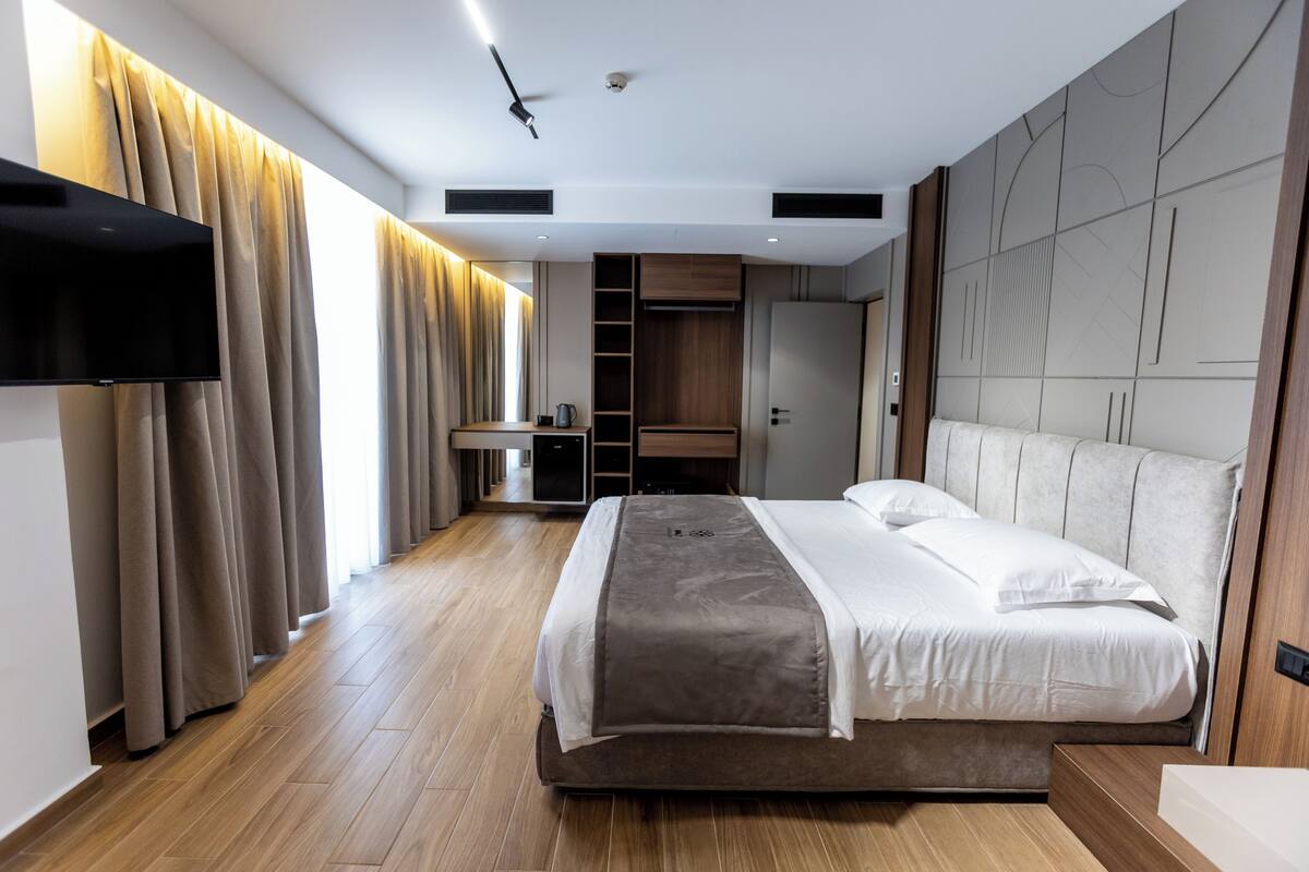 A modern hotel room with a large bed, a flat-screen TV mounted on the wall, and a wardrobe with built-in shelves.