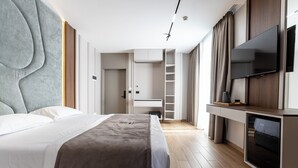 A modern hotel room with a large bed, a TV mounted on the wall, a wardrobe, and a built-in shelf. - Bolt Boutique Hotel (Shënkoll)