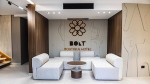 A modern hotel lobby with a central seating area, a prominent logo, and a staircase. - Bolt Boutique Hotel (Shënkoll)